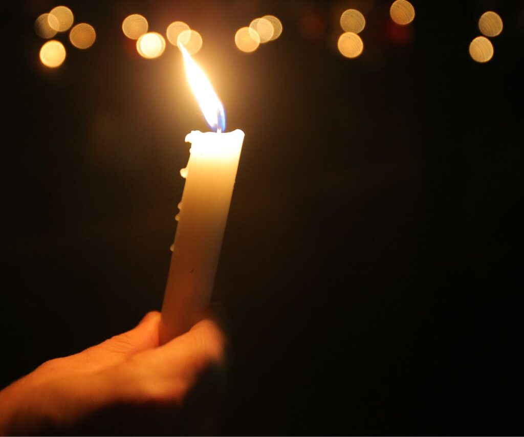 hand holding illuminated candle against black backdrop