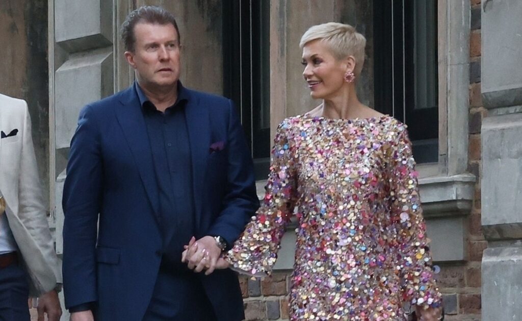 Jess, wearing a pink sequined dress, and Pete, in a blue suit, hold hands