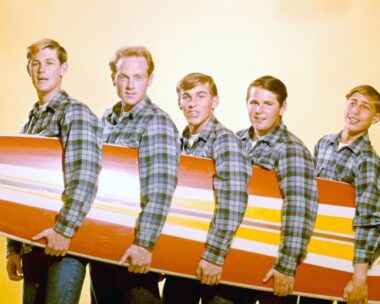 Vintage photo of the Beach Boys posing in plaid shirts holding a surfboard