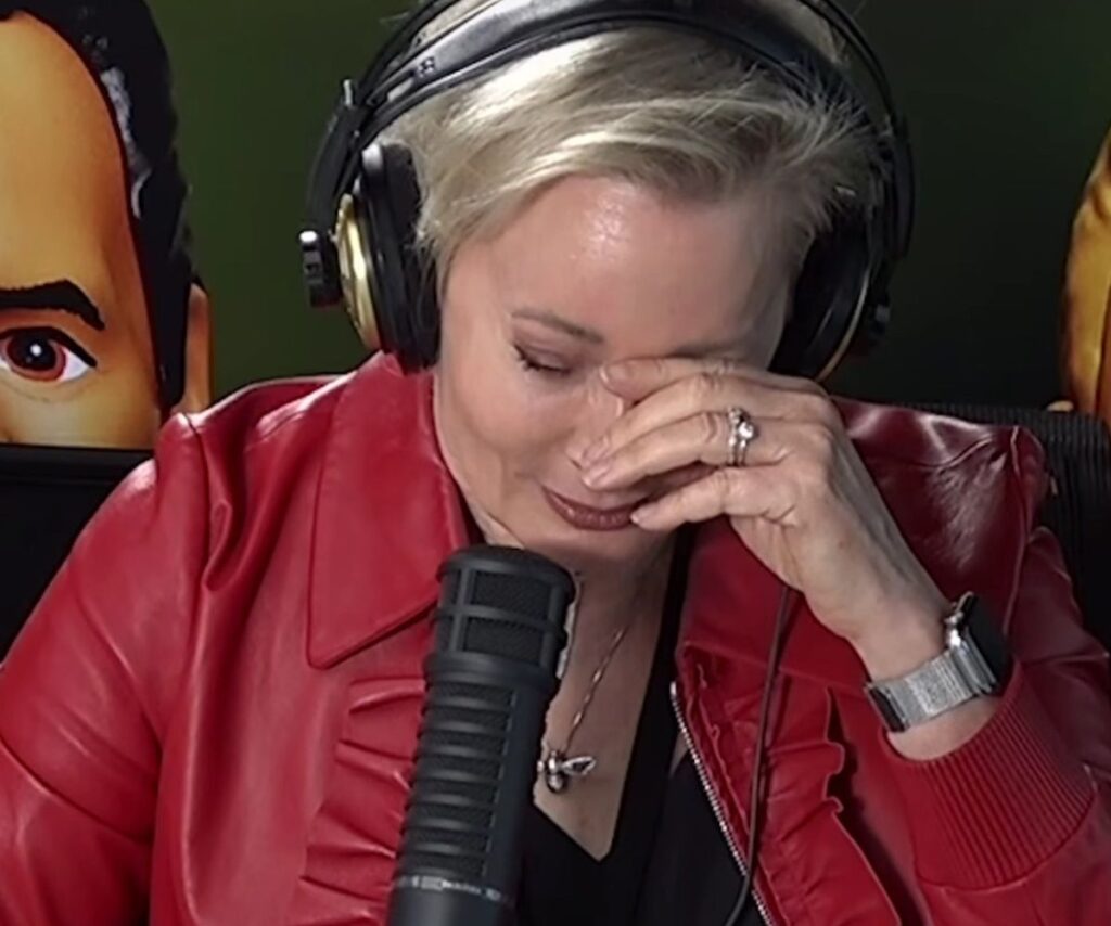 Amanda Keller wears red, hosting her show, overcome with emotion, hand to face, head angled down