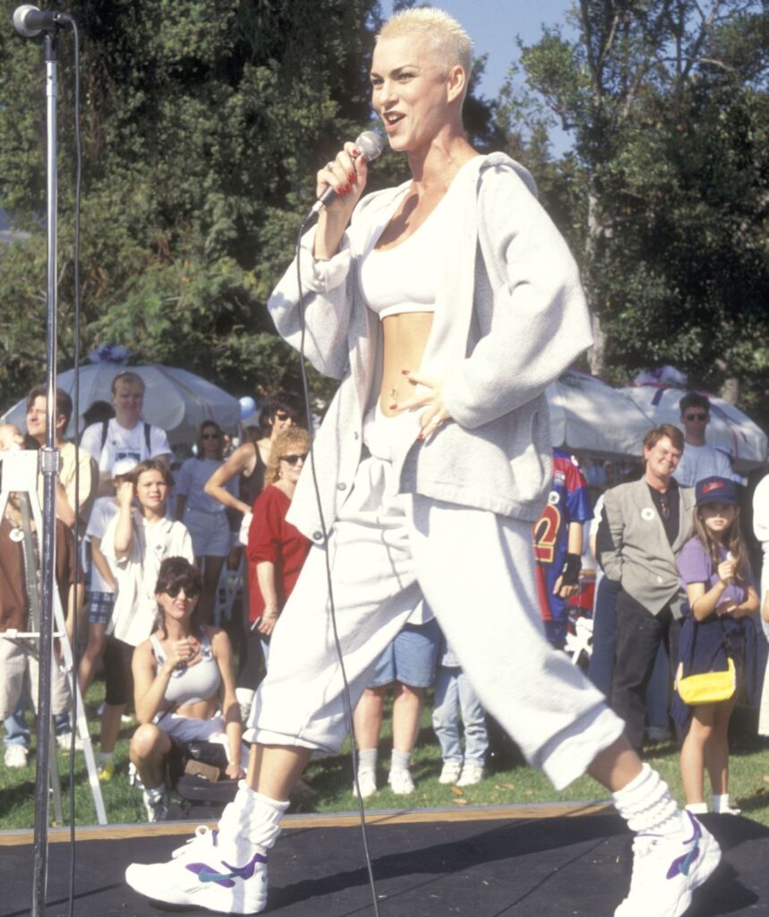 Susan Powter with short hair wearing all white on stage