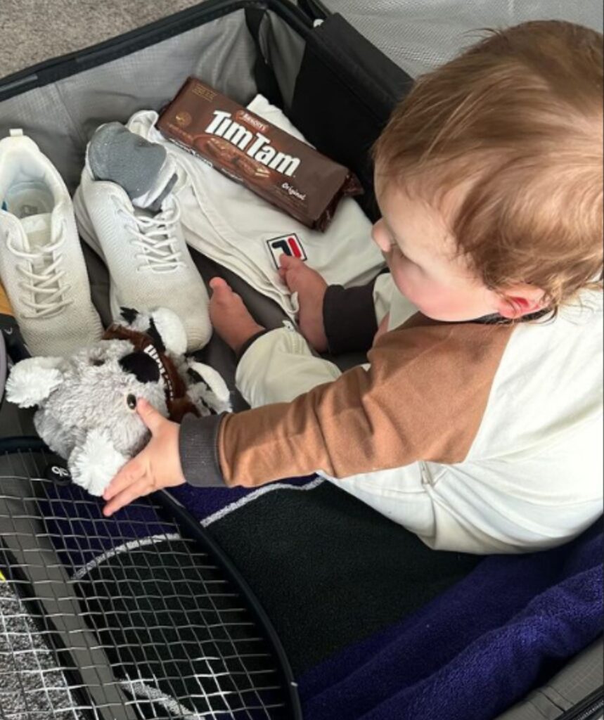 Ash Barty's son Hayden in a suitcase with tim tams and a tennis racquet