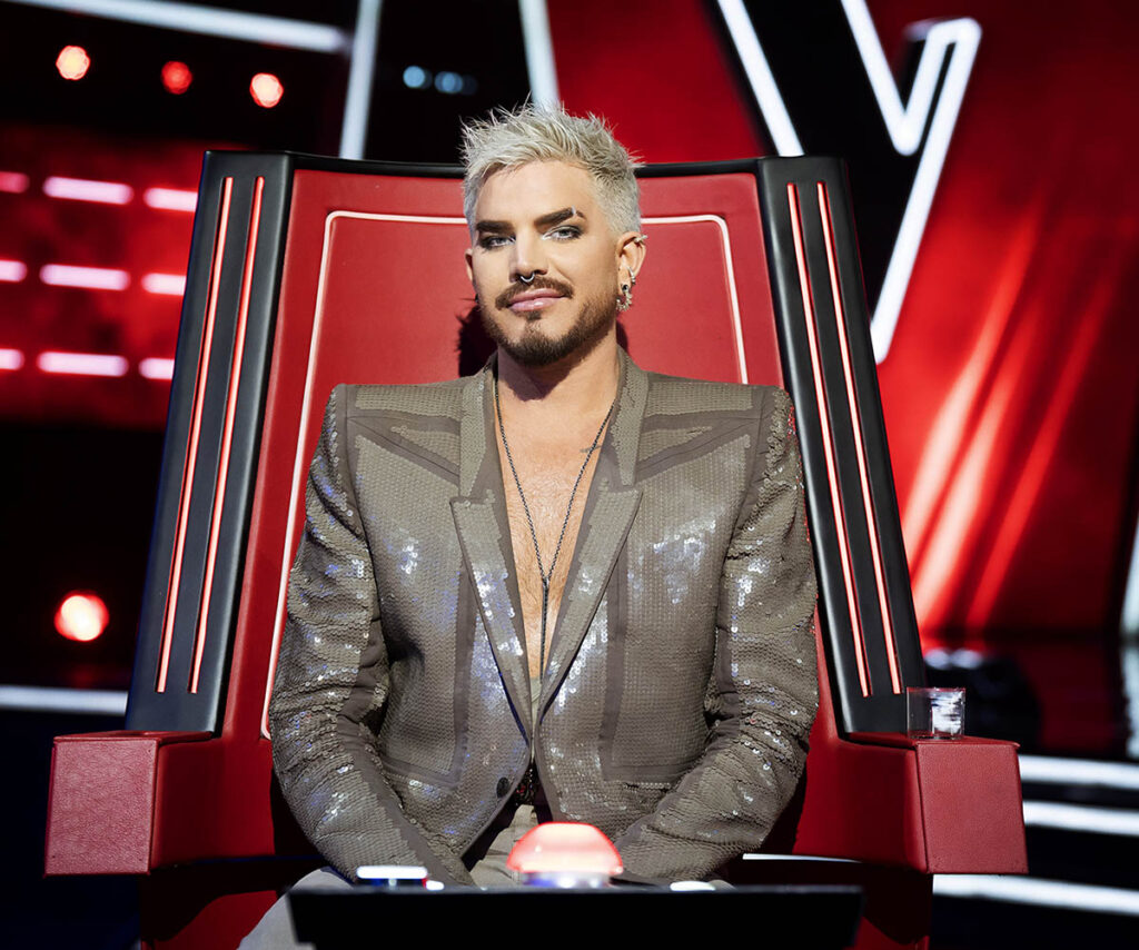 Adam Lambert sits in The Voice's iconic red chair.