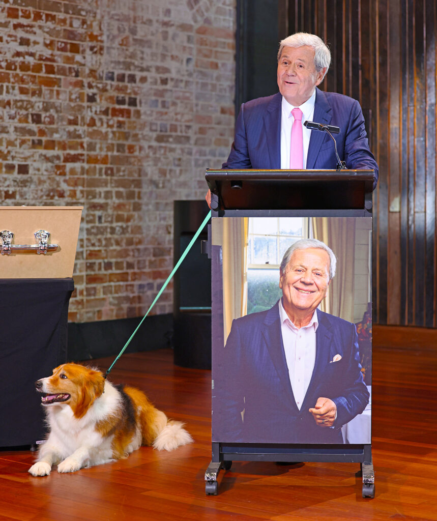 Ray stands at the podium with his dog to give a eulogy at his own fictional funeral in the show.