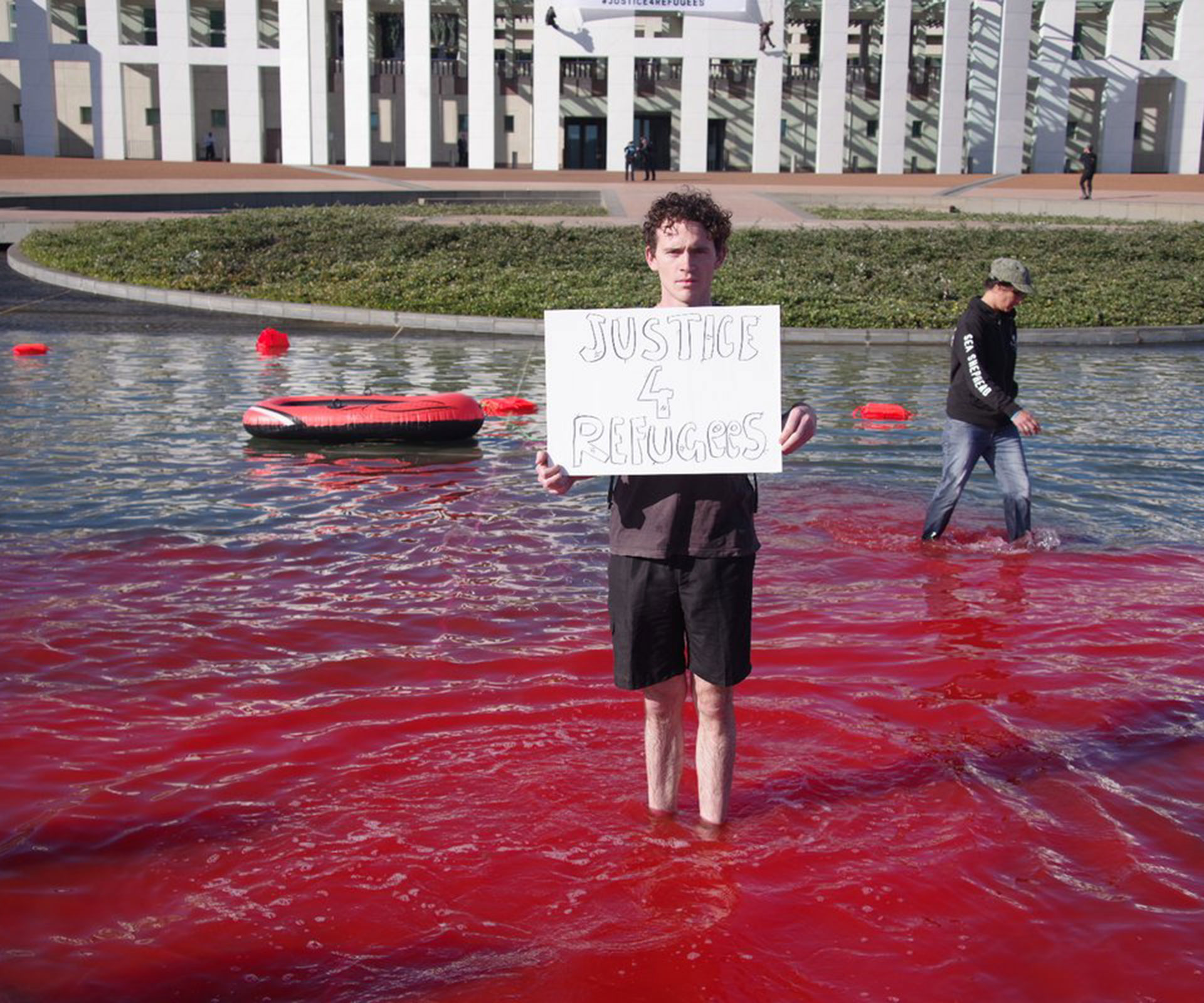 Pro-refugee campaigners abseiled down Parliament House and dyed the pond blood red in protest