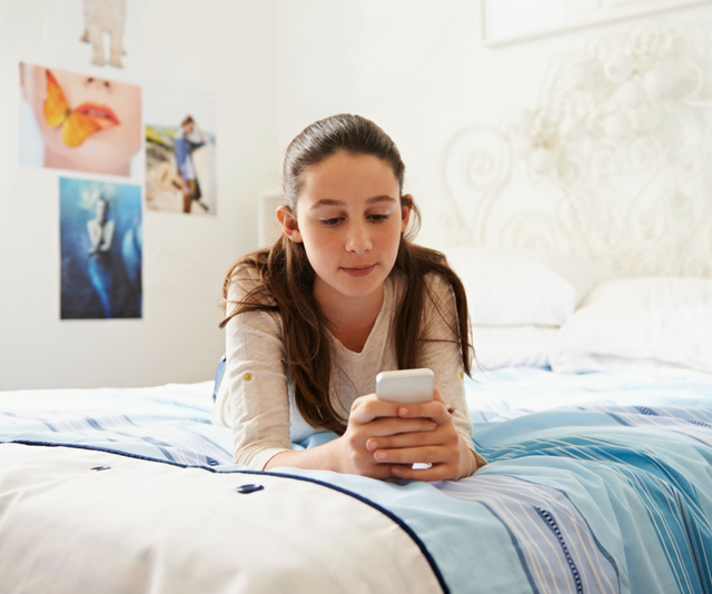 Young girl laying on bed swiping phone